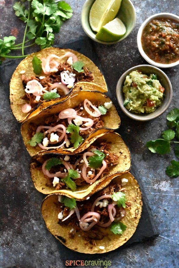 Four corn tortillas filled with crispy carnitas, garnished with onions, cotija cheese and cilantro