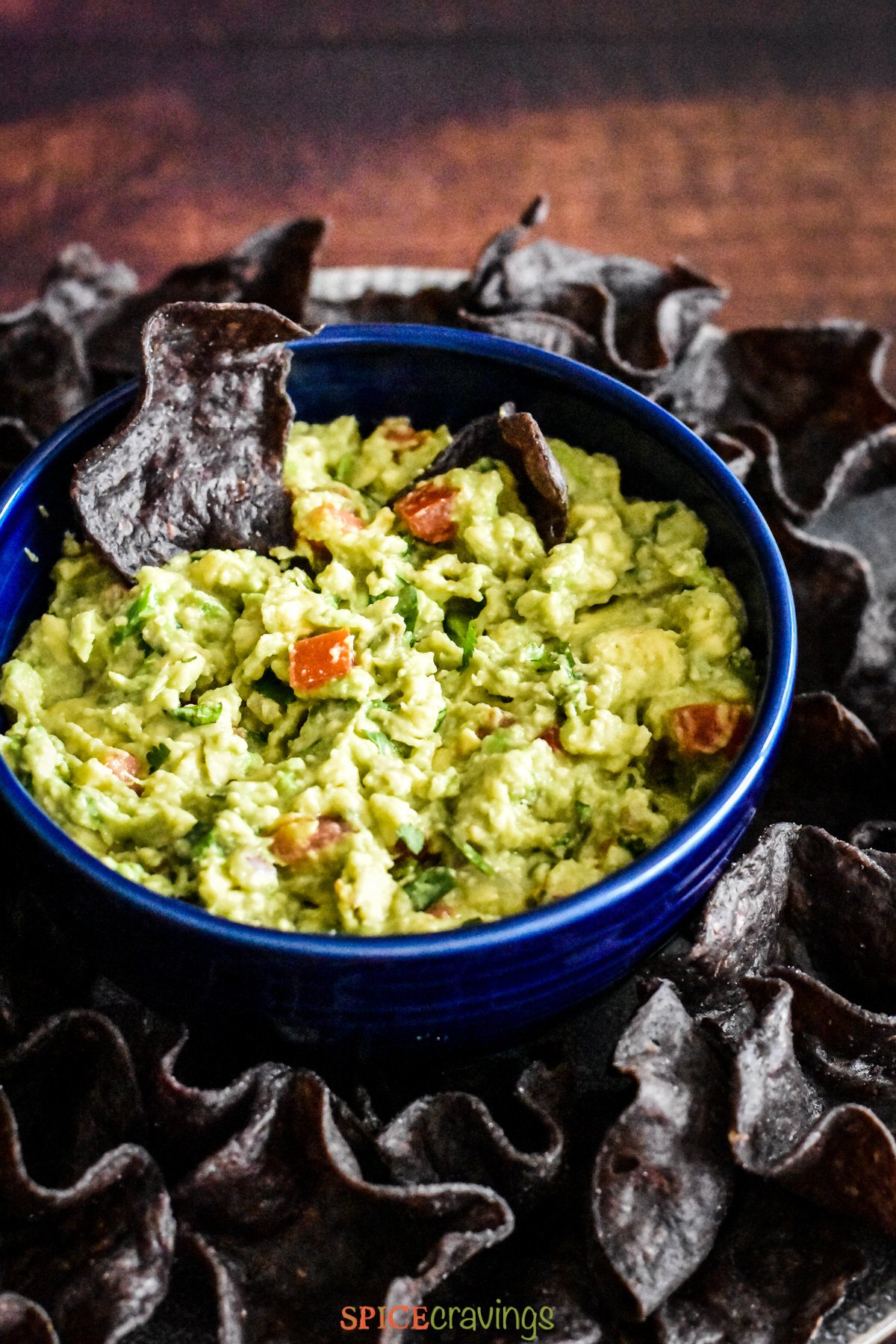 A bowl of fresg guacamole with blue corn chips served around
