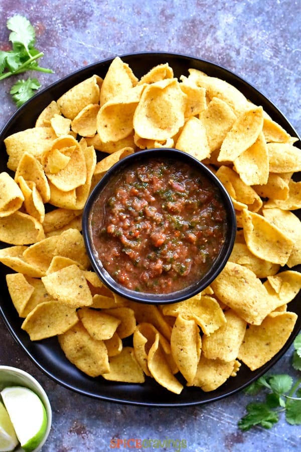 A plate of corn chips with a bowl of salsa in the middle