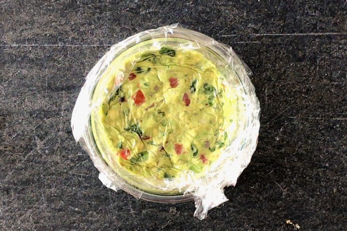 Pressing down plastic wrap to cover the surface of guacamole