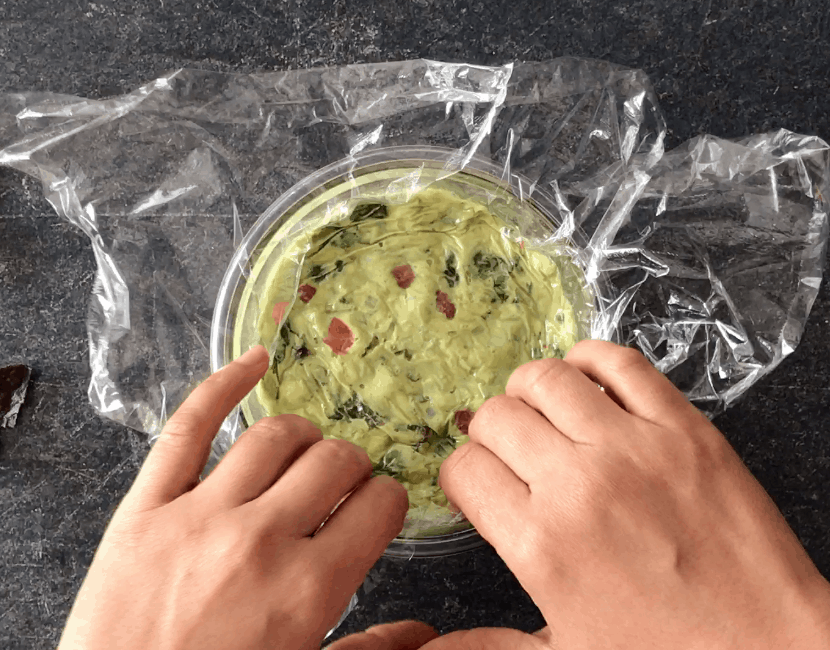 Pressing down plastic wrap to cover the surface of guacamole