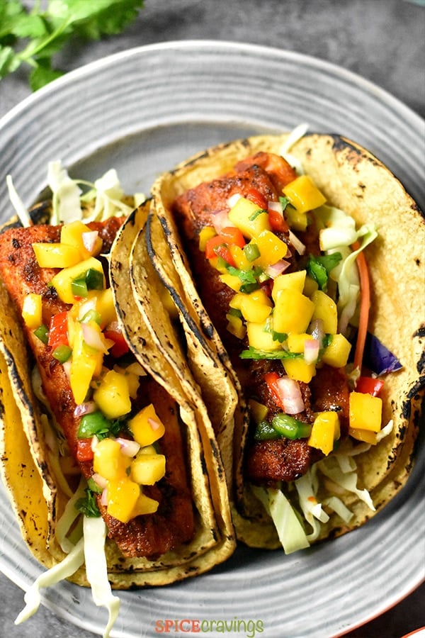 Two grilled fish tacos on a plate garnished with mango salsa