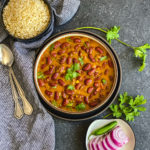 A bowl of Indian red beans curry with a side of brown rice and sliced onions