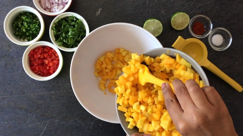 Adding chopped mango to a large mixing bowl