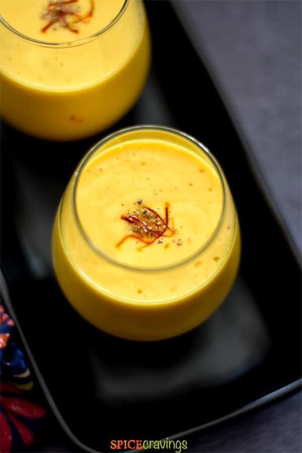 A glass of mango lassi garnished with saffron and ground cardamom