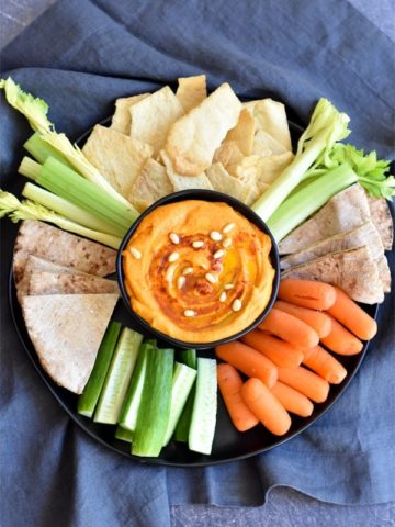 Red pepper hummus served with chips and veggies