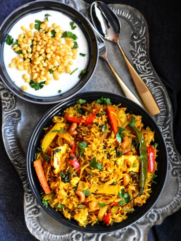 Bowl of Indian spiced vegetable biryani with a side of boondi raita