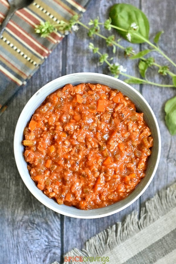 Chunky bolognese sauce served in a grey bowl, with basil on the side