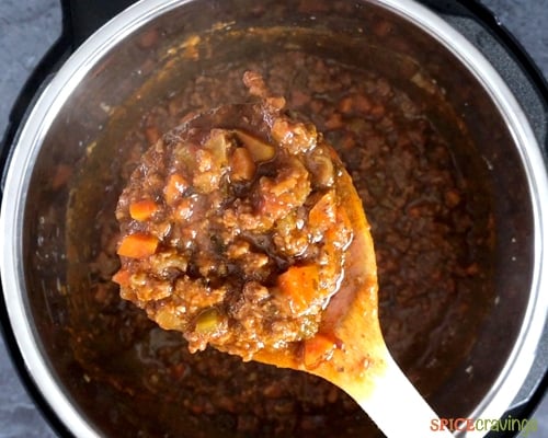 Chunky meaty bolognese sauce in a wooden spoon