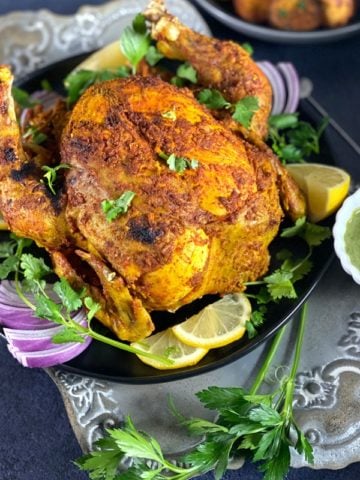 A whole roasted Tandoori Chicken on a grey platter