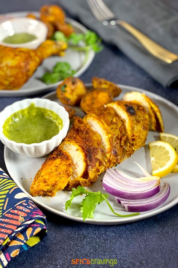 A plate of sliced tandoori Chicken with chutney and potatoes