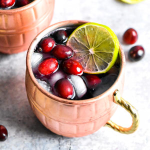 A copper mug with cranberry moscow mule, served with cranberries