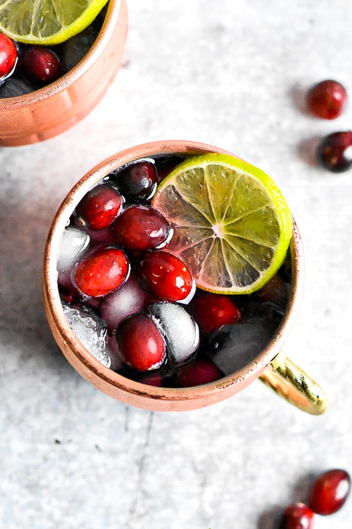 A copper mug with Moscow Mule topped with cranberries and lime