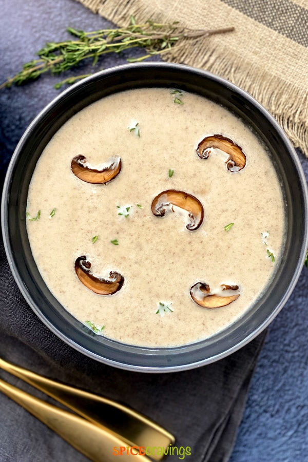 A blue bowl of mushroom soup garnished with thyme and mushrooms