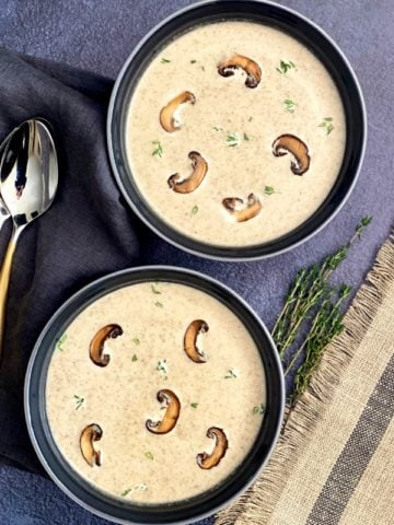 Two bowls with cream of mushroom soup garnished with thyme