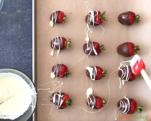 drizzling white chocolate over chocolate covered strawberries on parchment paper lined baking sheet