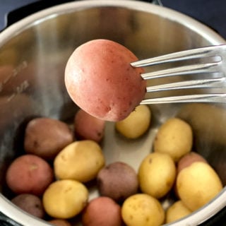 fork holding baby red potato over Instant pot with baby potatoes