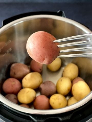 fork holding baby red potato over Instant pot with baby potatoes