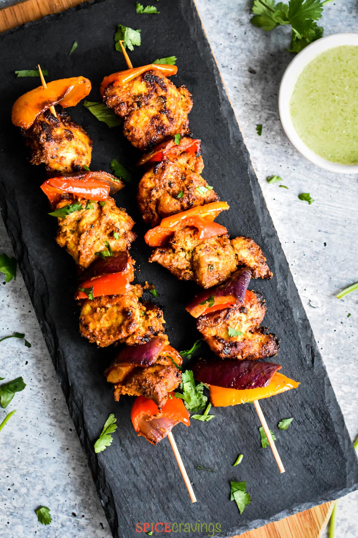 Two skewers of chicken tikka served on a gray slate