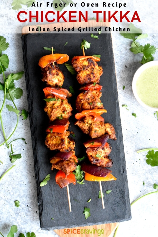 Two skewers of grilled Indian Chicken tikka on a slate tray