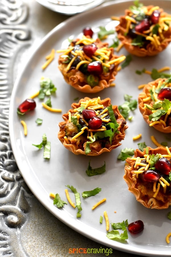 samosa chaat phyllo cups garnished with cilantro, pomegranate seeds and thin sev on white plate