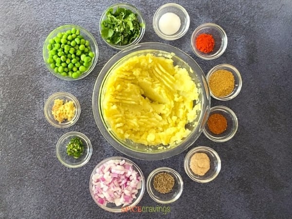 mashed potatoes in large glass bowl with peas, onions and spices in small glass bowls in a circle