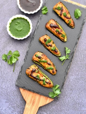 baked samosa stuffed jalapeno poppers on charcoal board with cilantro and tamarind chutney in two white bowls