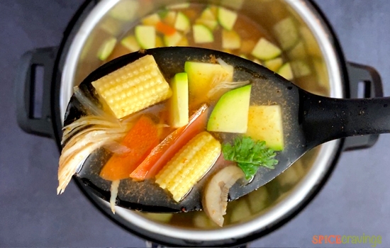 A ladle with Tom Yum Soup with baby corn, zucchini, carrots and chicken