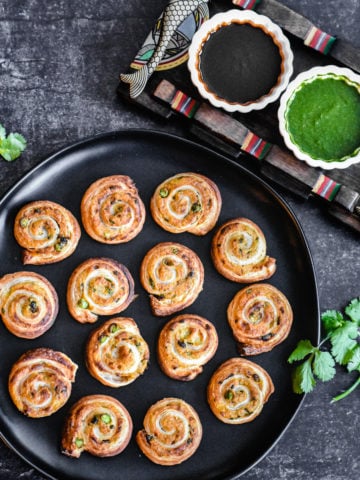 puff pastry samosa pinwheels on black serving plate with cilantro and tamarind chutney in two small white bowls