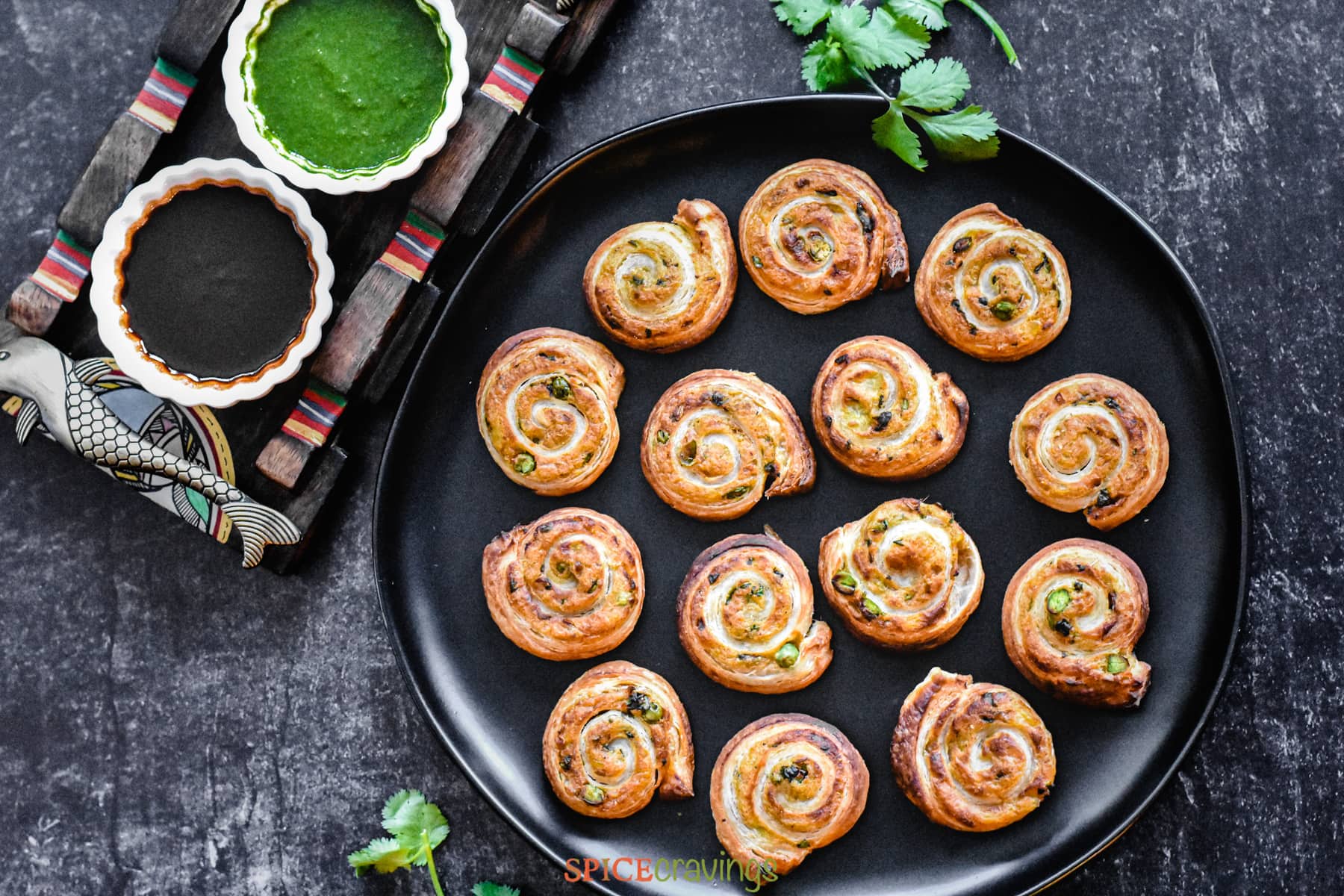 Puff pastry pinwheels on black plate next to Indian chutney