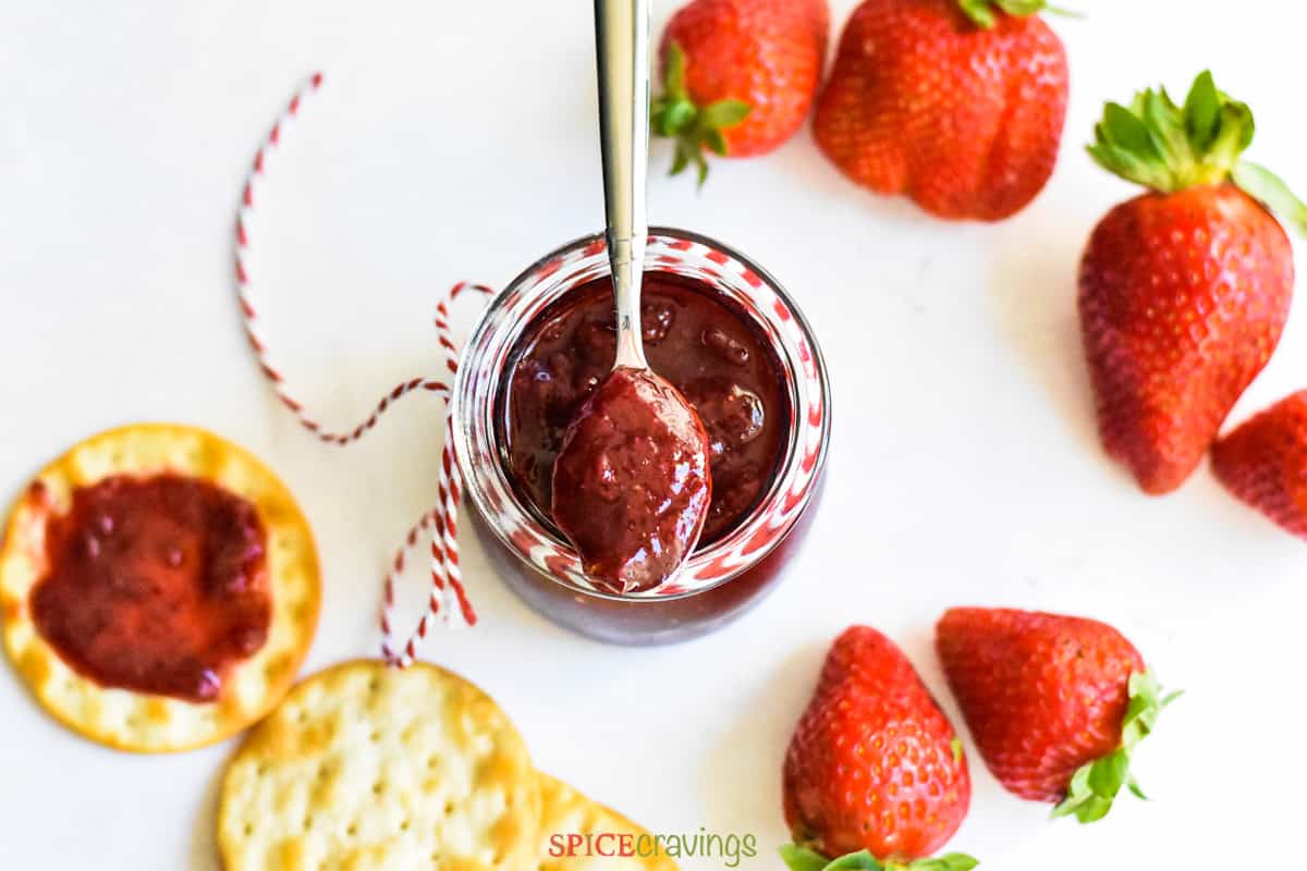 freezer strawberry jam in glass jar with silver spoon with fresh strawberries