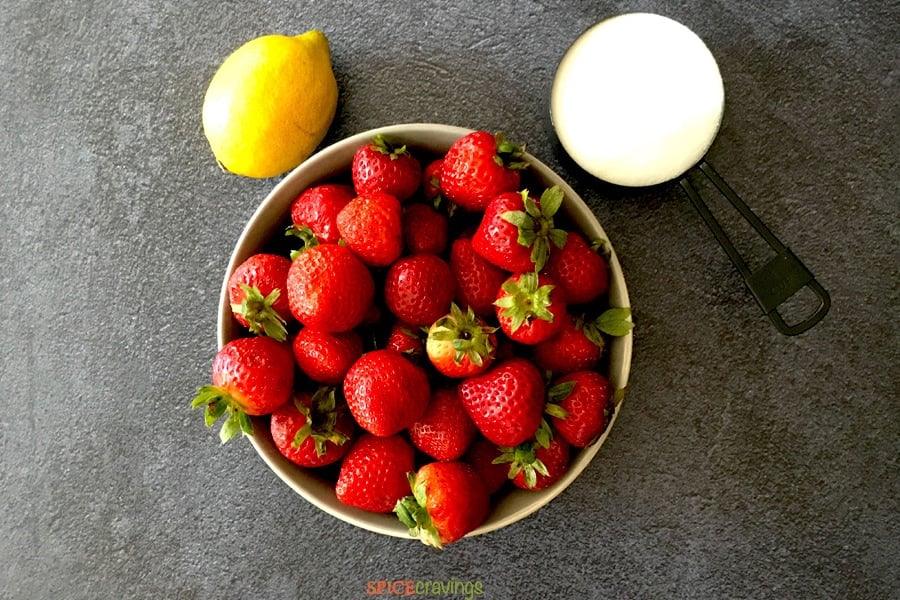 fresh strawberries in white bowl, lemon, sugar in measuring cup