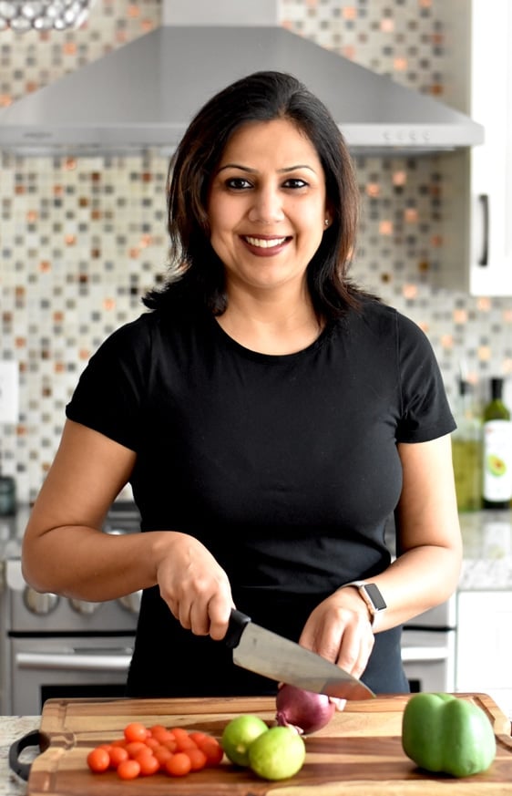 Author of Spice Cravings shown cutting an onion on a wooden cutting board