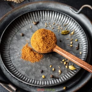 ground spice blend in wooden spoon on metal trays with whole spices around