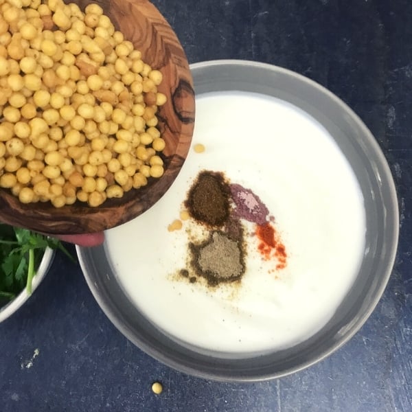 pouring boondi into gray bowl with yogurt and spices