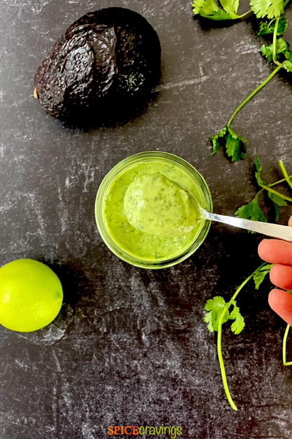 green and creamy cilantro lime salad dressing in small mason jar with spoon and avocado