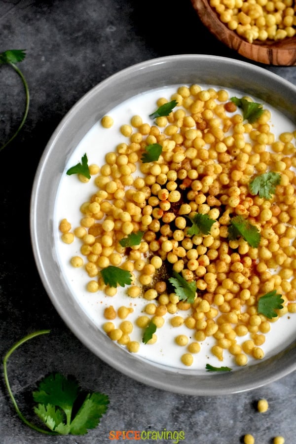 spiced yogurt condiment with fried chickpea flour fritters garnished with cilantro in gray bowl