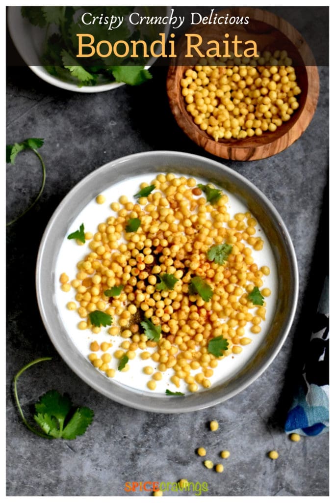 spiced yogurt sauce with fried chickpea balls in gray bowl with boondi and cilantro on the side