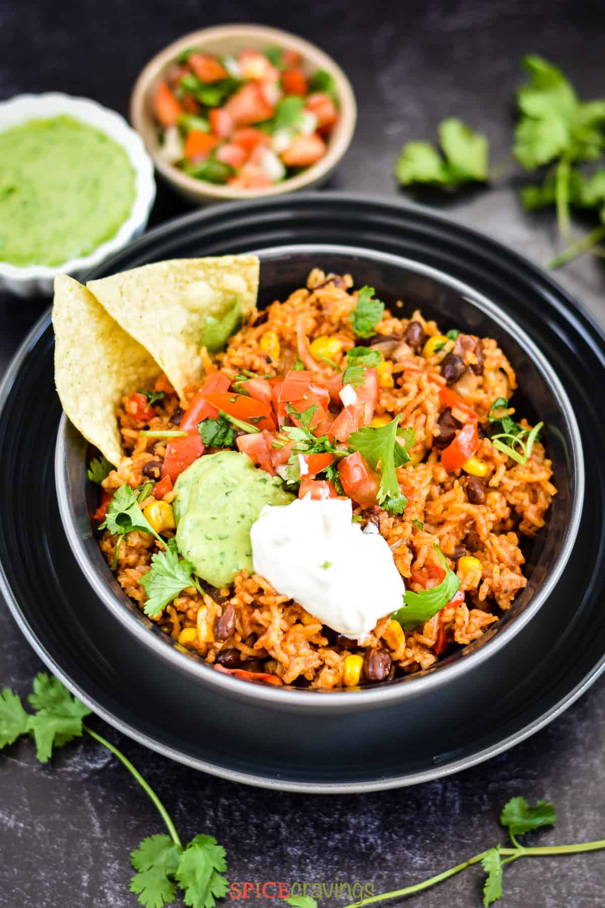 authentic Mexican rice and black beans in black bowl with tortilla chips and sour cream