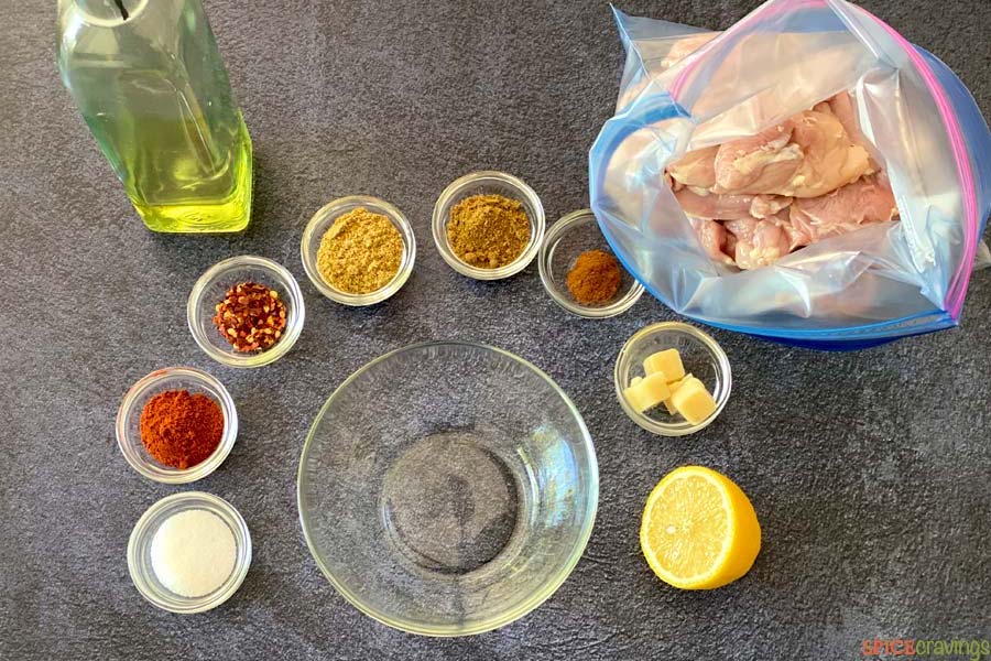 spices in small bowls, olive oil in glass bottle, chicken in ziplock bag