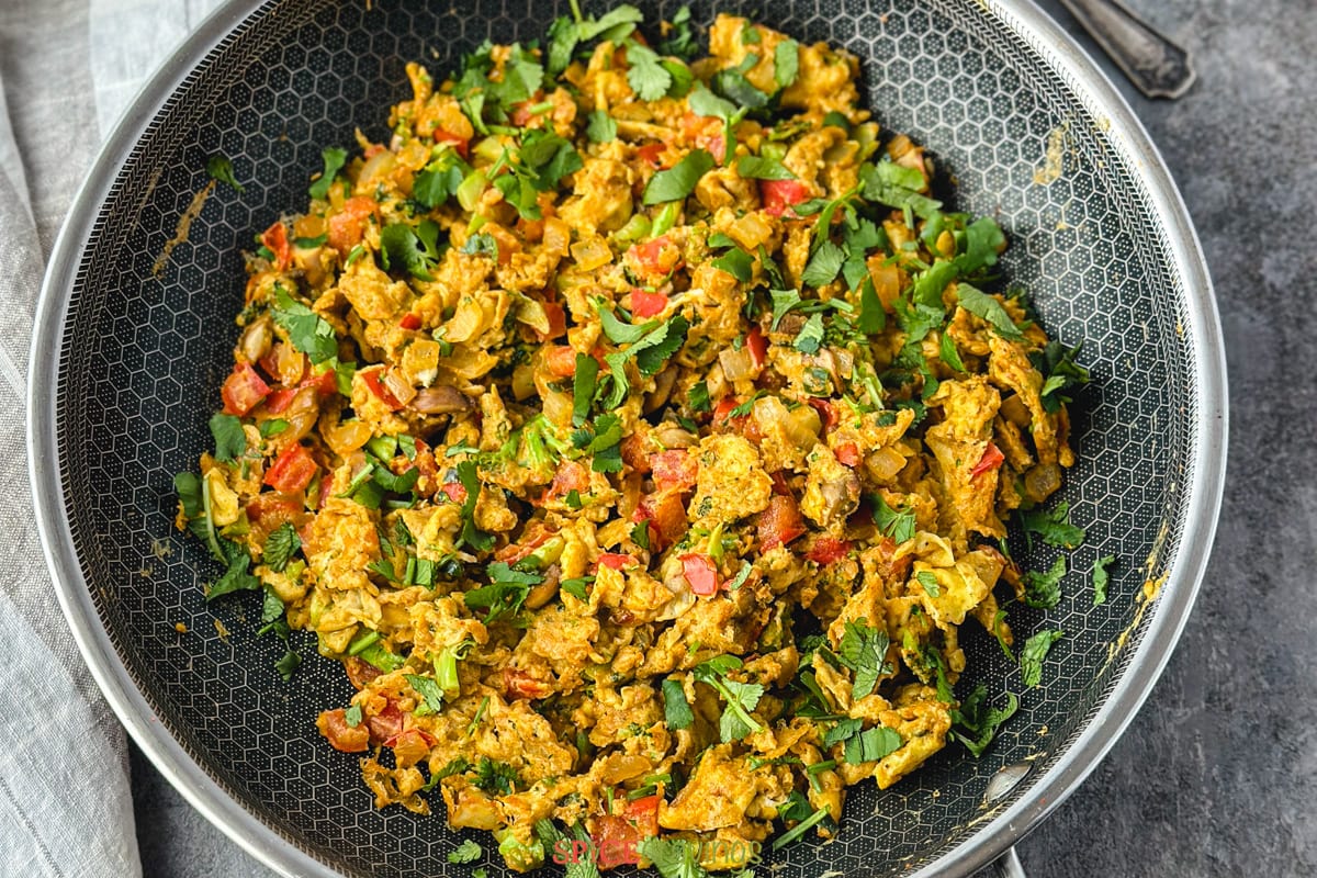 Indian scrambled eggs in non-stick skillet with red spatula