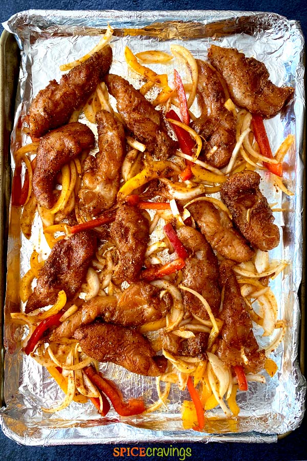 seasoned chicken, onions and bell peppers on foil lined sheet pan