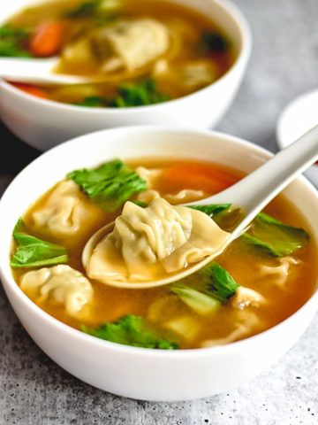 Two bowls of soup with dumplings, spinach and carrots
