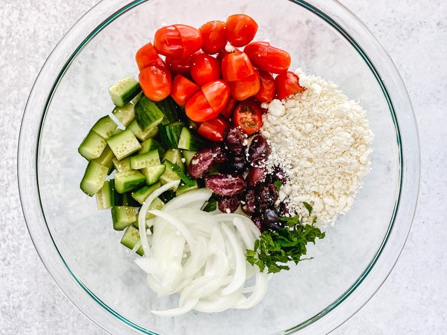 diced cucumbers, tomatoes, onions, olives, feta cheese, herbs in glass bowl