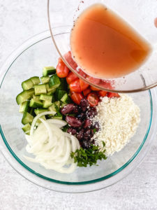 red wine dressing pouring over chopped greek salad