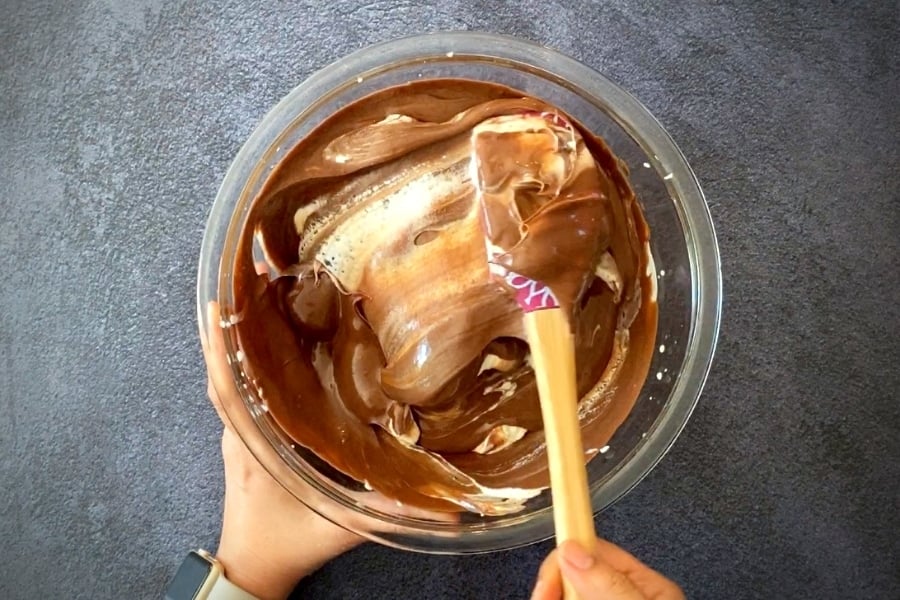 two hands folding chocolate into whipped cream with spatula