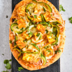 indian flatbread pizza with marinated paneer cheese and veggies on black board