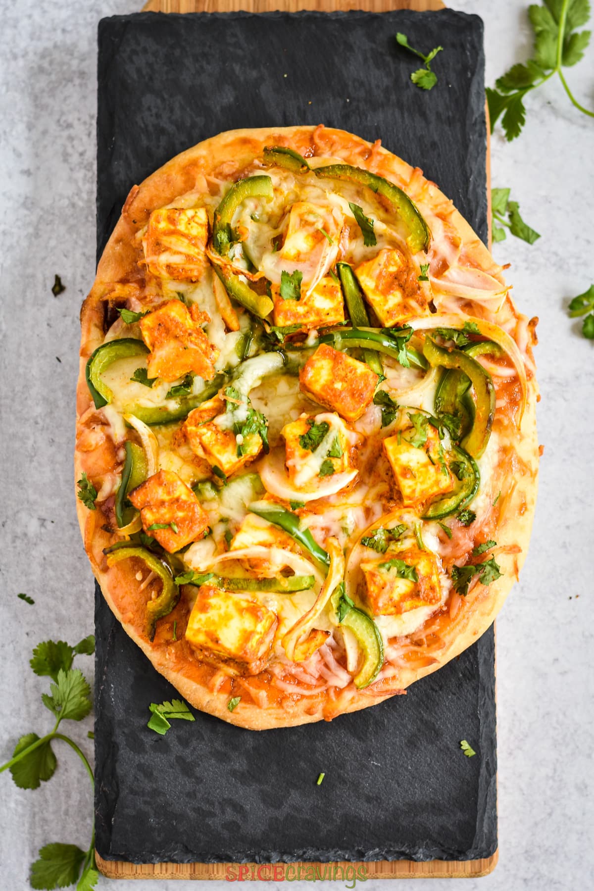 indian flatbread pizza with marinated paneer cheese and veggies on black board