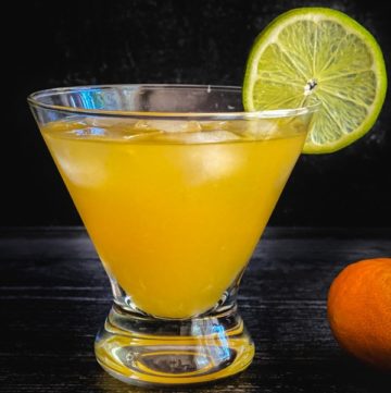An orange cocktail garnished with a lime wheel