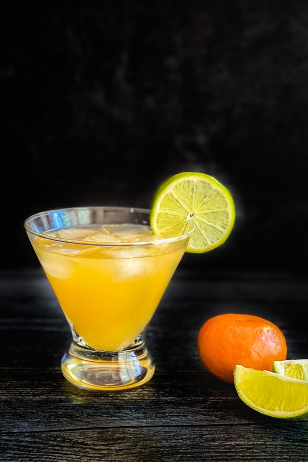 A glass of orange margarita garnished with a lime slice